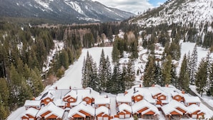 Un groupe de petites cabanes en bois rouge, aux toits couverts de neige, entourées d’une forêt et de montagnes.