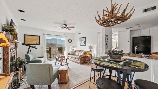 A modern living room with a fireplace, a dining area with a round table, and a kitchen with a large TV. - Full Kitchen Mountain Views Indoor Pool Access (Gatlinburg)