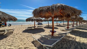A beach with thatched umbrellas and lounge chairs. - Luxury New Oceanfront Condo 5BR Sleeps 12 (Puerto Peñasco)