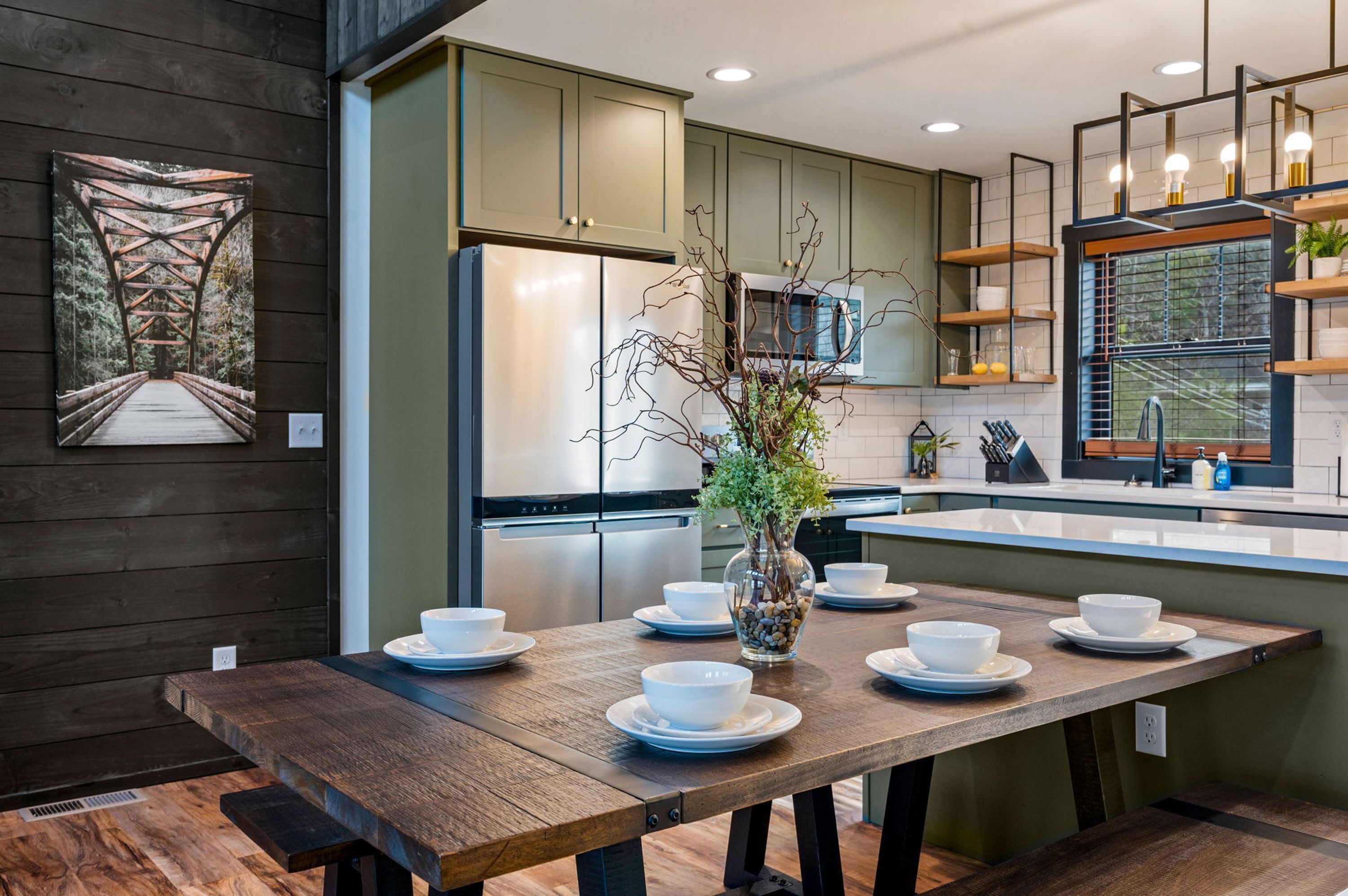 Una cocina moderna con armarios de madera, un refrigerador de acero inoxidable, una mesa de comedor con tazones y platos, y un florero con plantas.
