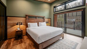 Un dormitorio con cabecera de madera, un ventanal grande y una mesita de noche con lámpara.