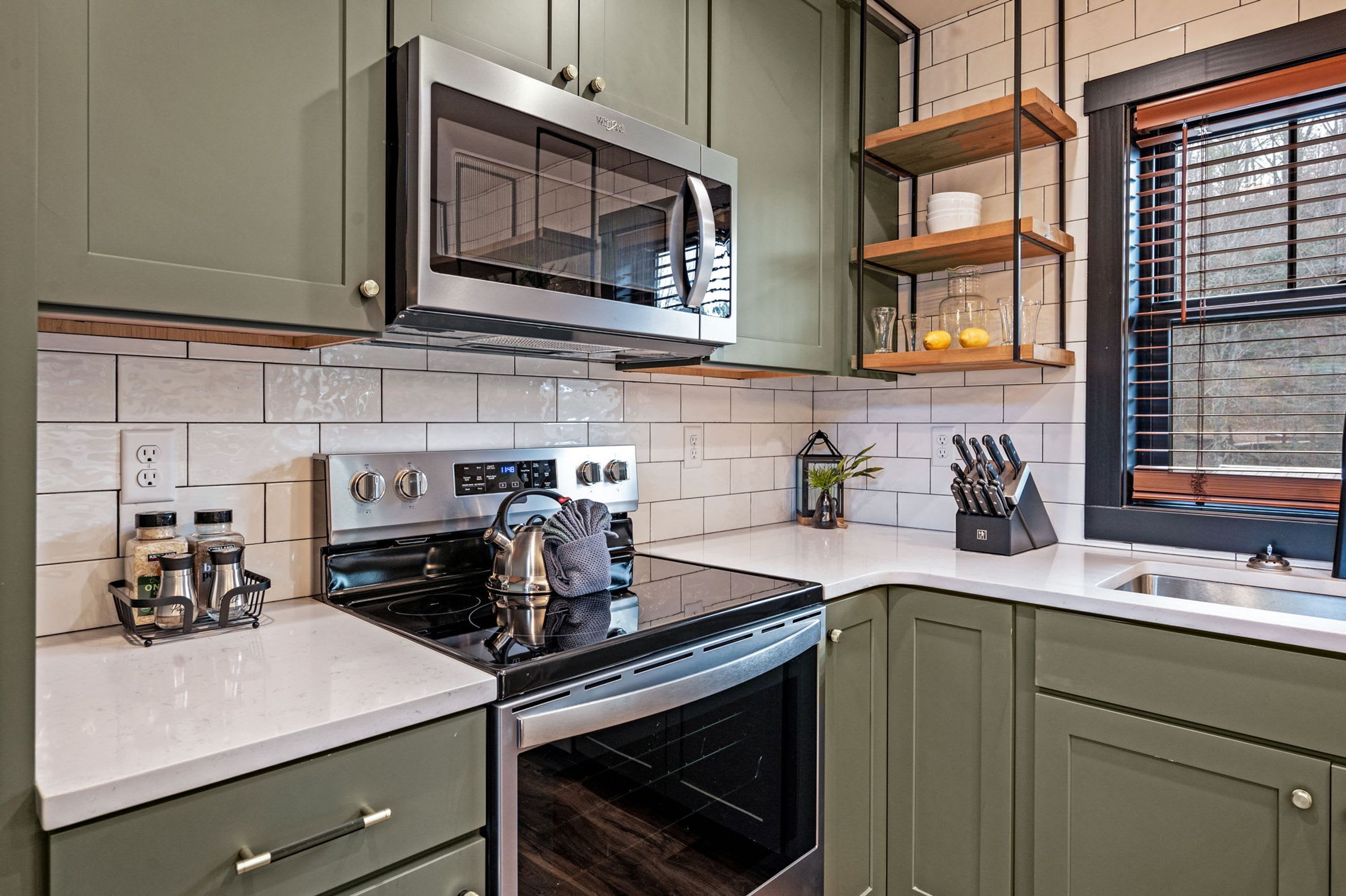 A kitchen with a built-in microwave, stove, oven, and a window with blinds.