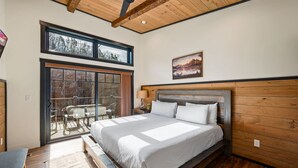 Un dormitorio con una cama grande, vigas de madera en el techo, vistas a una zona de estar exterior por una puerta corrediza y un cuadro en la pared.