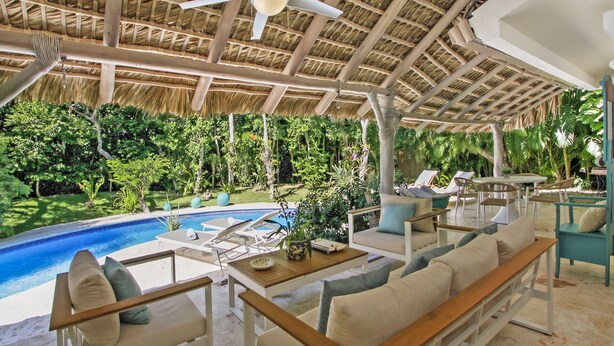 Un área de lounge al aire libre con piscina, asientos y techo de paja.