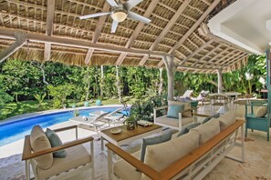 An outdoor lounge area with a pool, seating, and a thatched roof. - Large Family 2 Level Villa for Rent at Puntacana Resort Club Near Playa Serena Playa Blanca (Punta Cana)