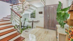 Una escalera con escalones de madera y baranda de metal, una puerta de madera y una planta verde grande.