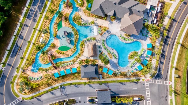 An aerial view of a resort with a large swimming pool, a water slide, and a parking area.