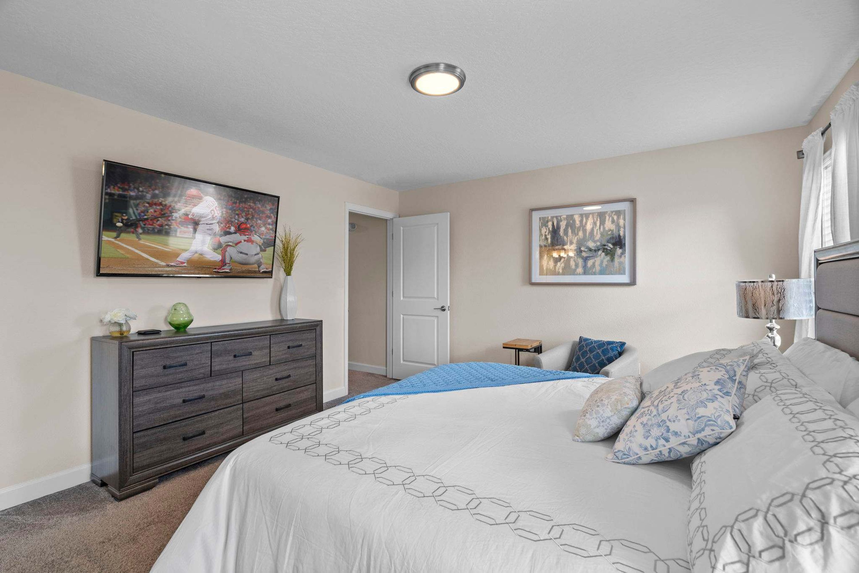 A bedroom with a large bed, a dresser, a painting, and a door.
