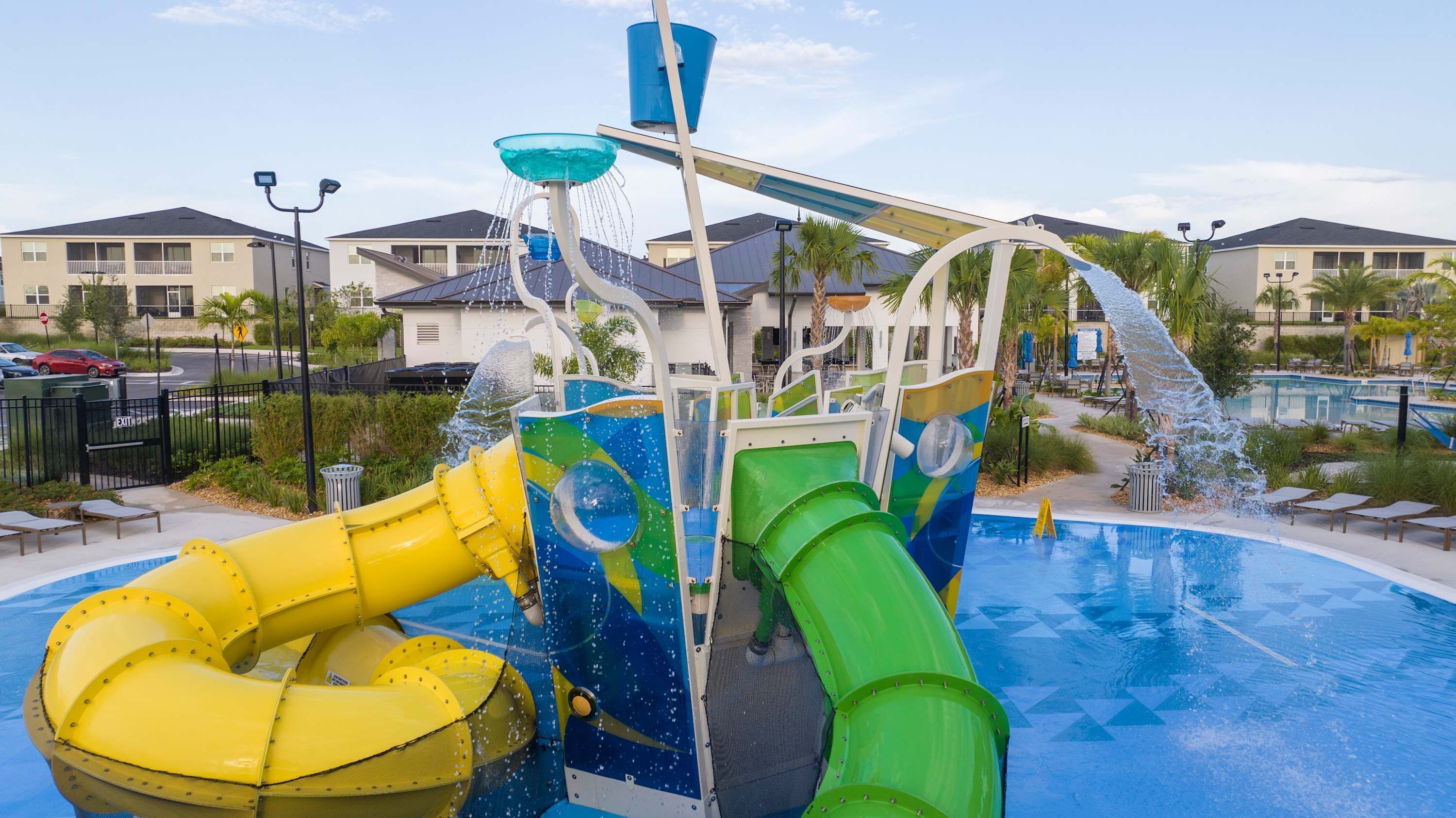 Parque acuático con una piscina grande, un tobogán de agua amarillo y verde, y una fuente.
