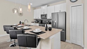 A modern kitchen with white cabinets, stainless steel appliances, and a central island with seating. - Magical Getaway in the Best Location for a Perfect Vacation (Davenport)