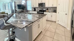 A modern kitchen with white cabinets, a granite island, and a built-in microwave.