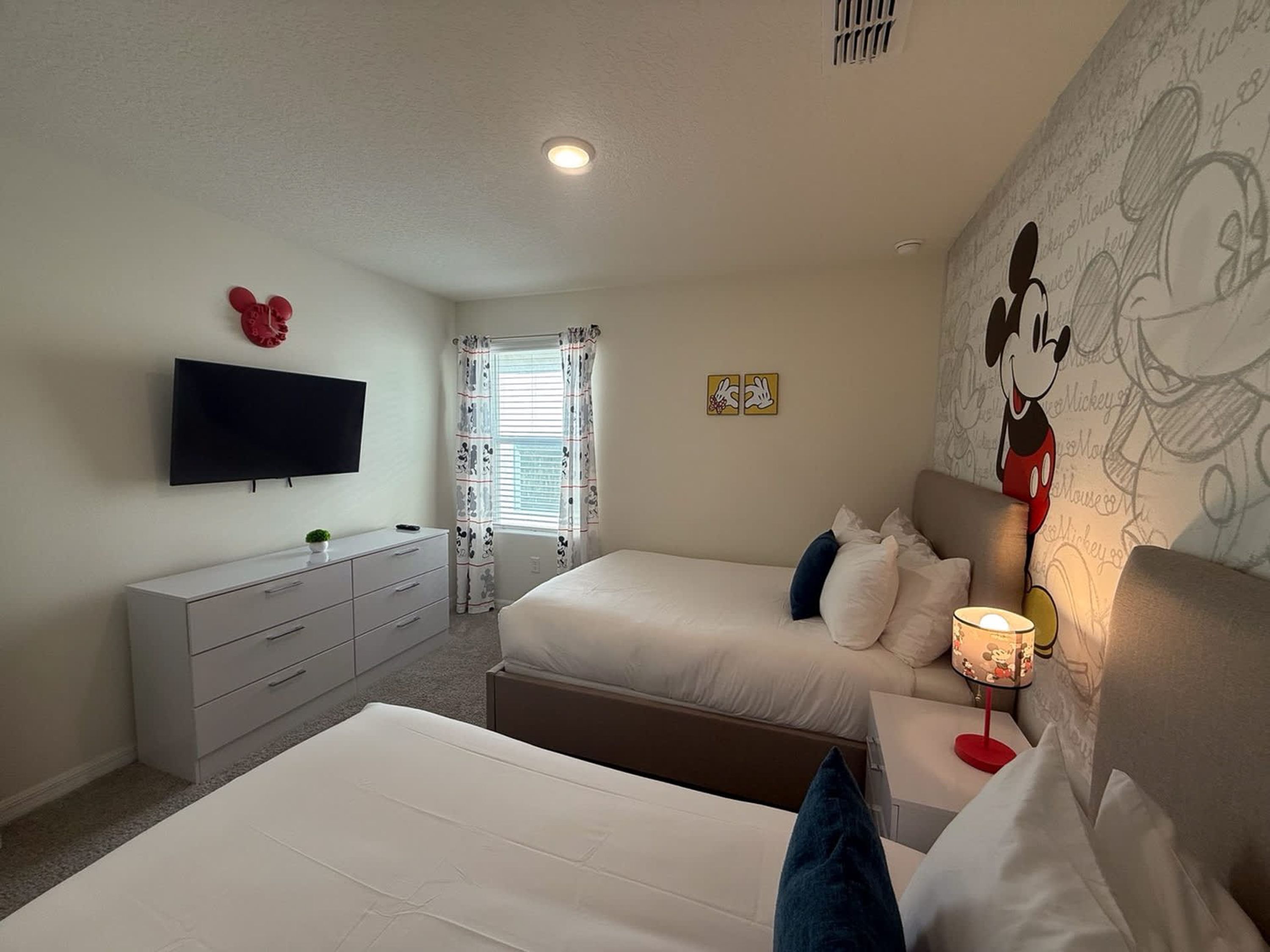 A bedroom with two beds, a TV, a dresser, and Mickey Mouse wallpaper.