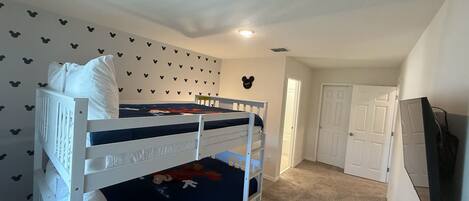 Un dormitorio con dos literas, una puerta blanca y una pared decorada con pegatinas de Mickey Mouse.