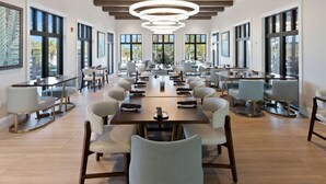 A spacious dining area with multiple tables and chairs, large windows, and a modern chandelier.