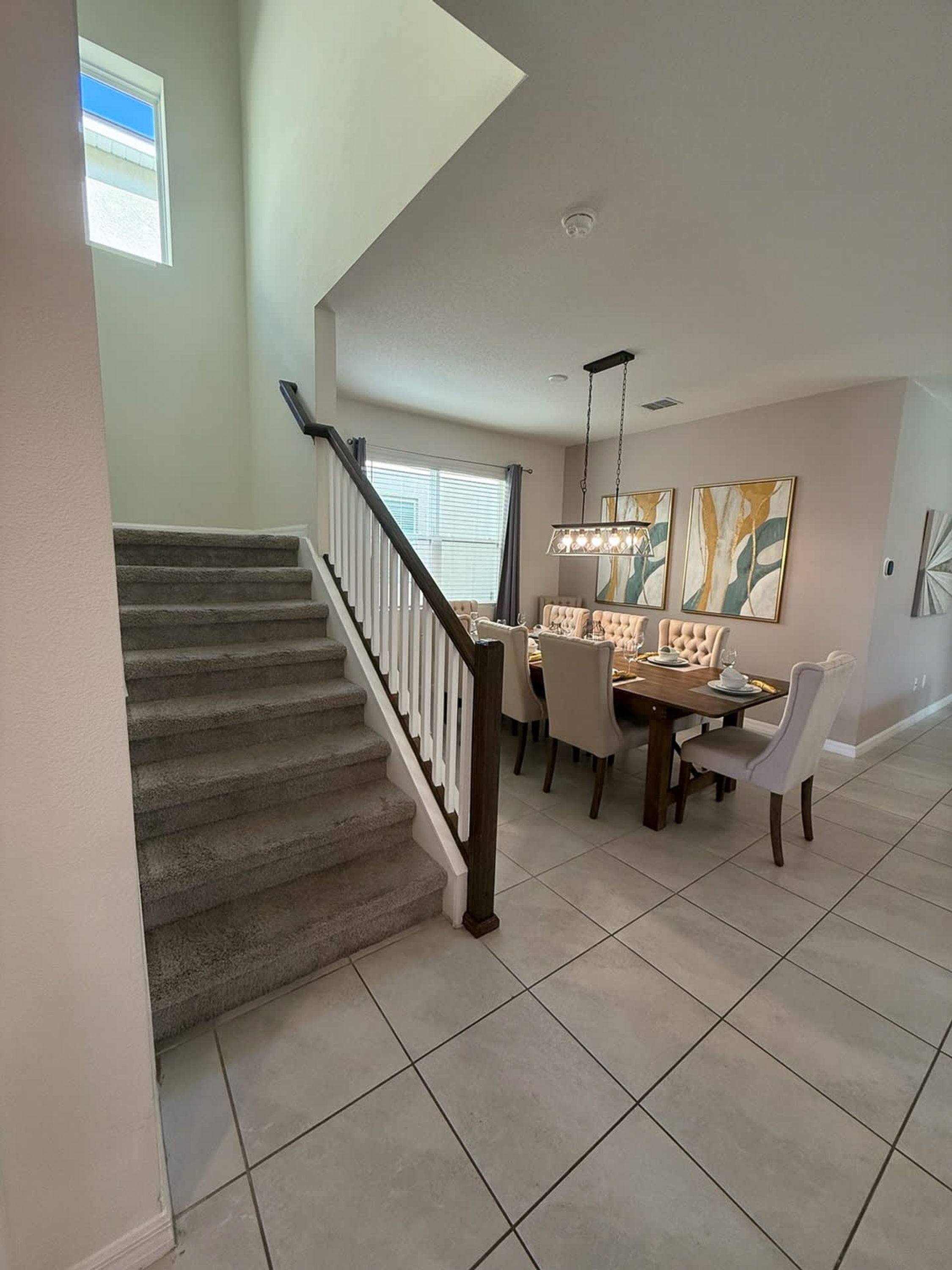 A dining area with a staircase, a chandelier, and abstract wall art.