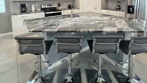 A modern kitchen with white cabinets, a large island with bar stools, stainless steel appliances, and pendant lighting.