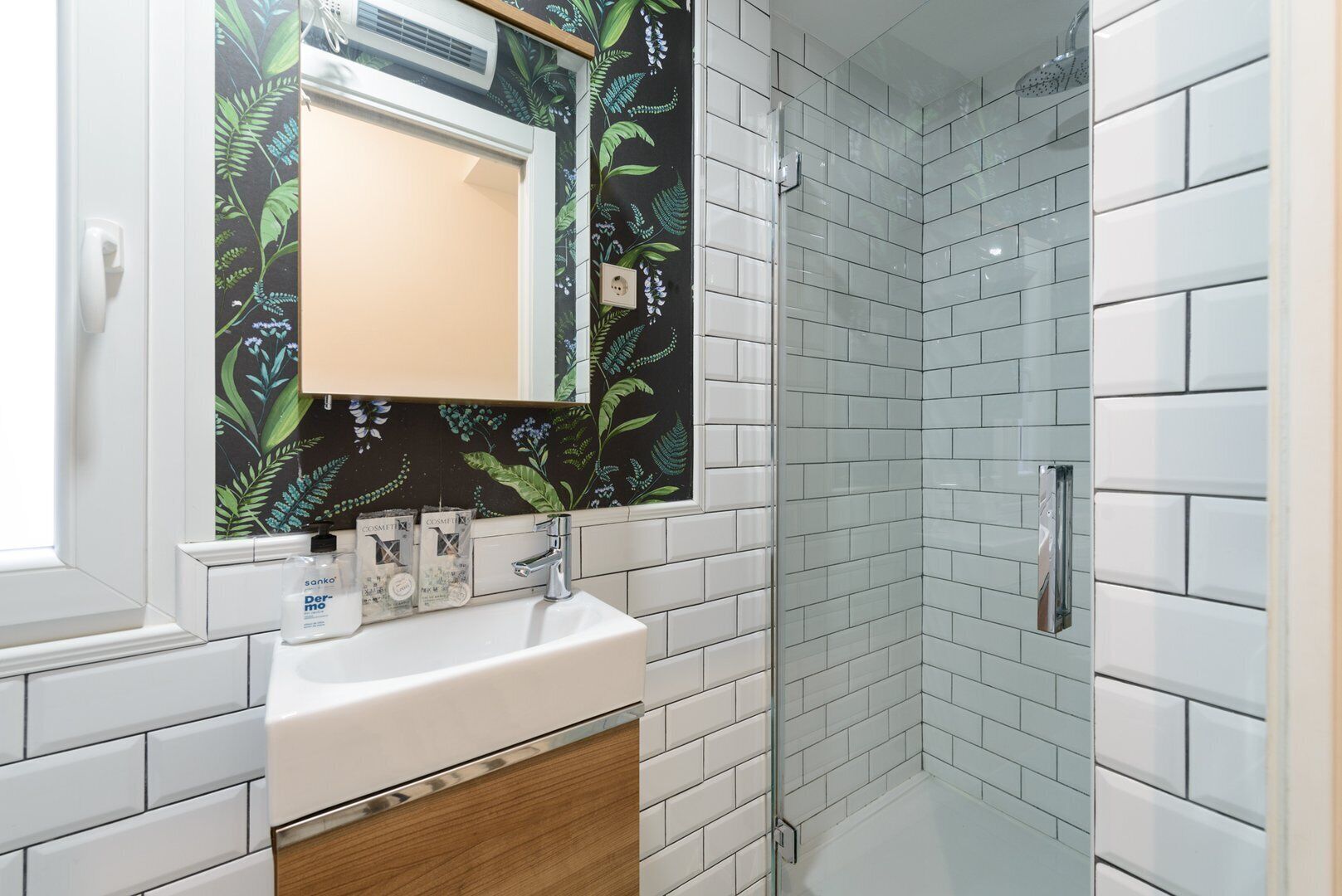 Un baño con un lavabo blanco, un espejo y una zona de ducha con azulejos blancos.