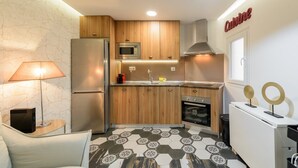 A compact kitchen with wooden cabinets, a microwave, a refrigerator, and an oven. There's a sink with a faucet, a lamp, and a decorative wall sign. - GuestReady - A lovely home near Plaza Mayor (Madrid)