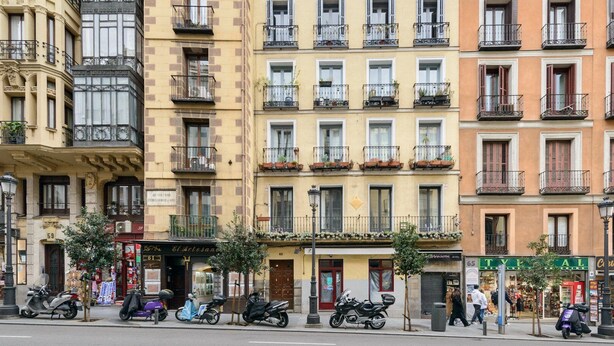A row of multi-story buildings with balconies, storefronts, and parked scooters. - GuestReady - A lovely home near Plaza Mayor (Madrid)