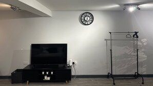 A modern living room with a flat-screen TV on a black stand, a wall-mounted clock, and a ceiling-mounted light fixture. - Cozy Studio In The City Centre by Luxesuites (Sheffield)