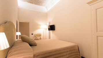 Una camera d'albergo con un letto, una sedia, una TV a parete e una lampada.