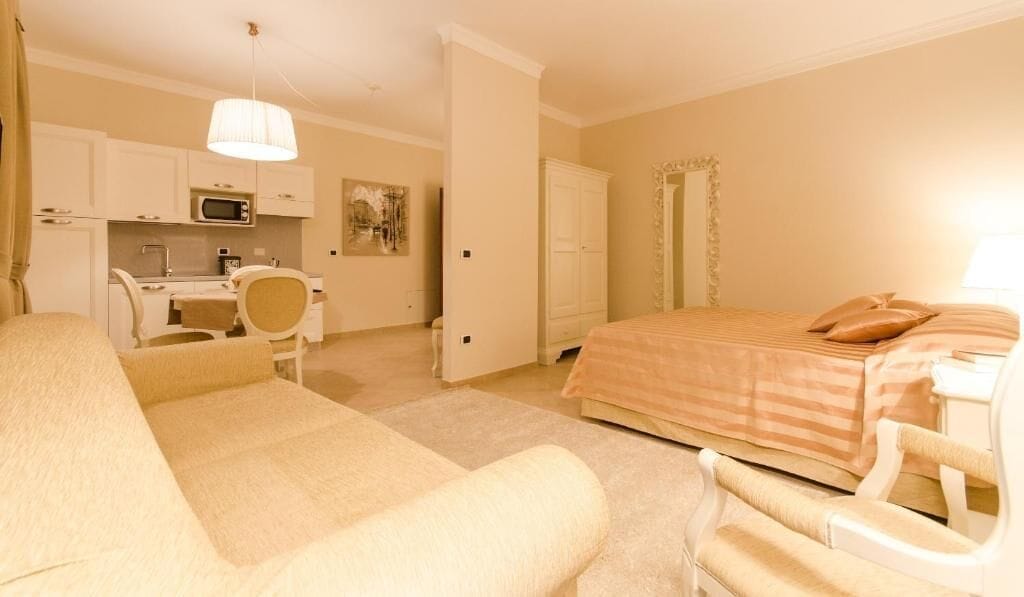 A hotel room with a bed, a desk, a chair, a sofa, and a kitchen area.