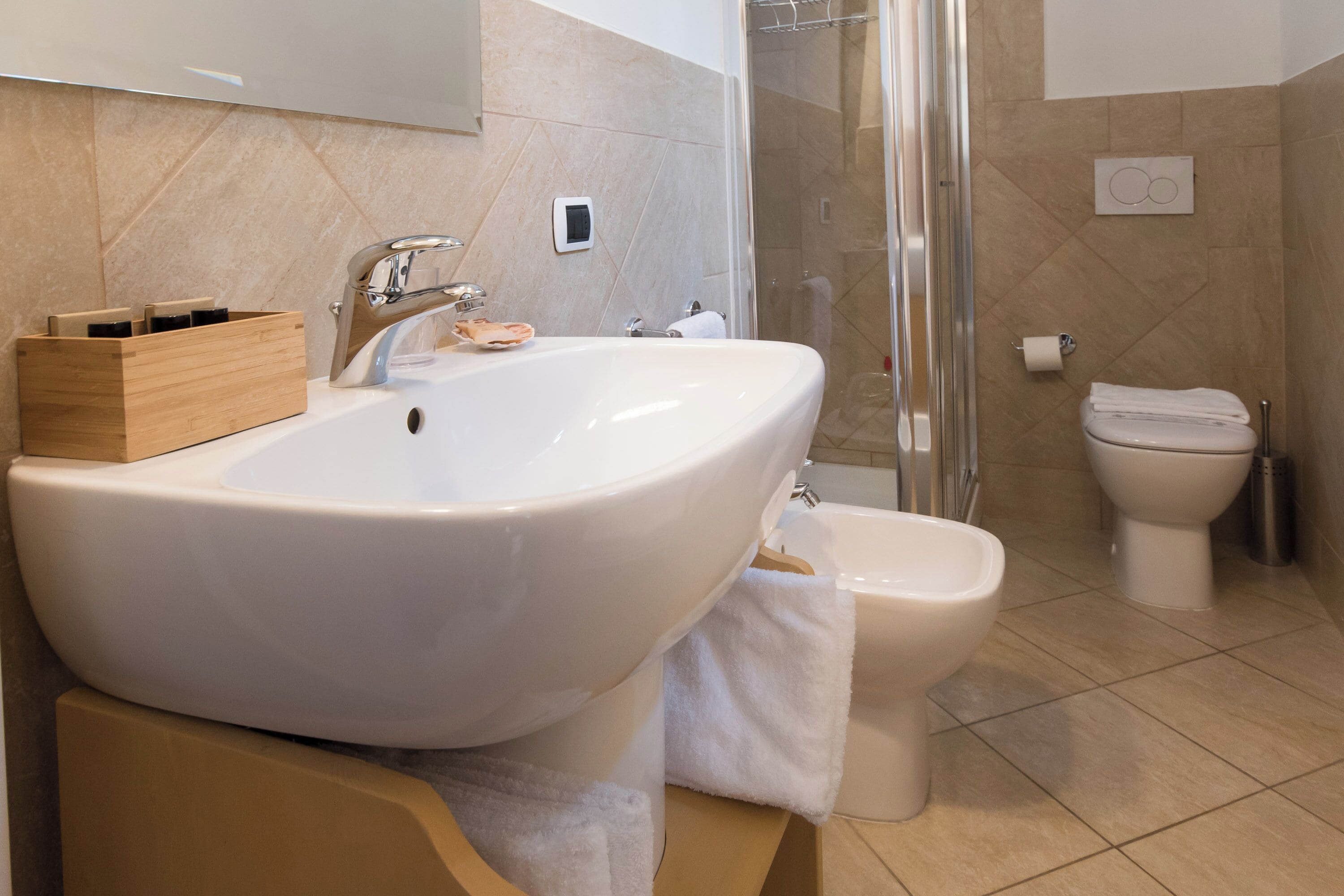 A modern bathroom with a large white sink, a toilet, and a glass-enclosed shower.