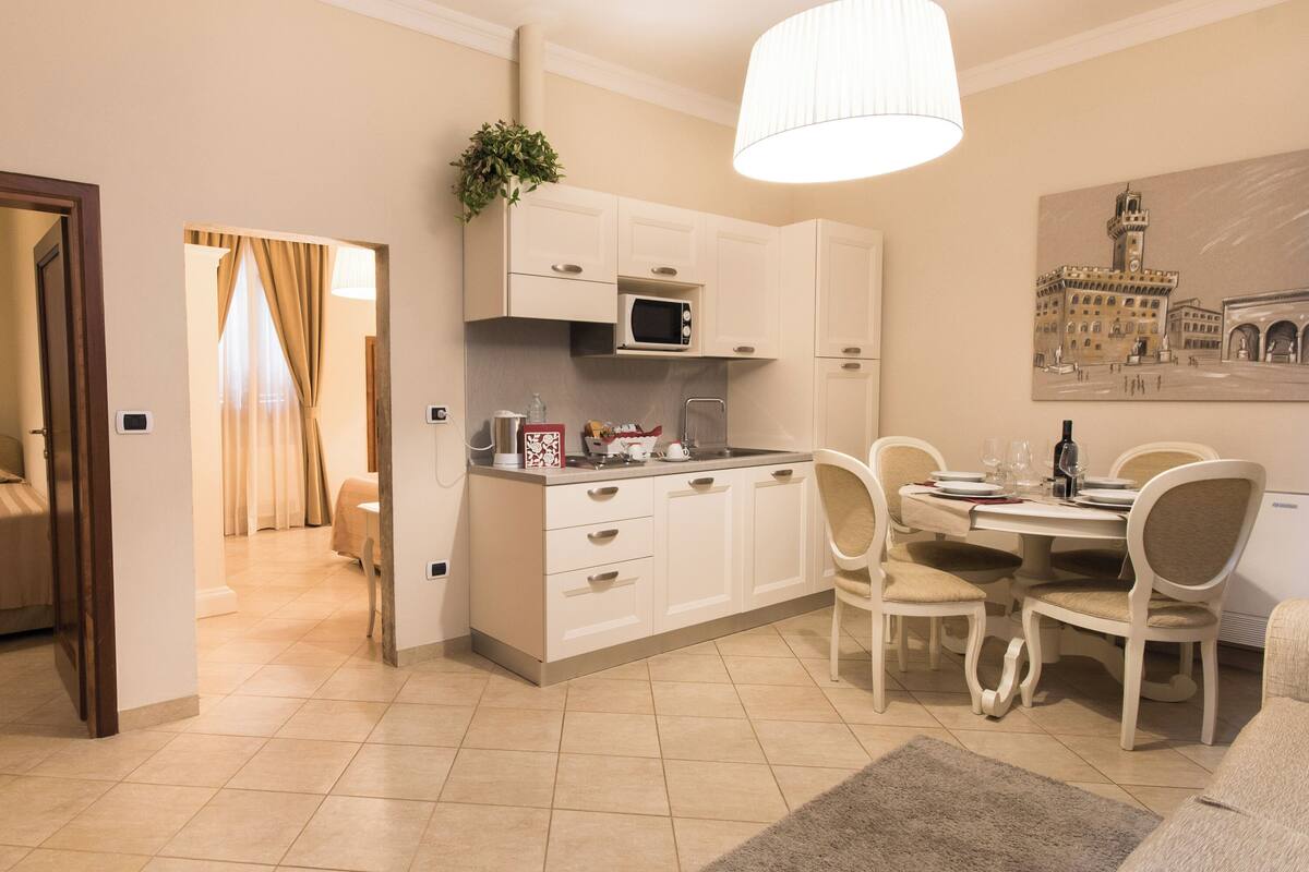 Een moderne keuken met witte kastjes, een magnetron, en een eethoek met stoelen en een tafel.