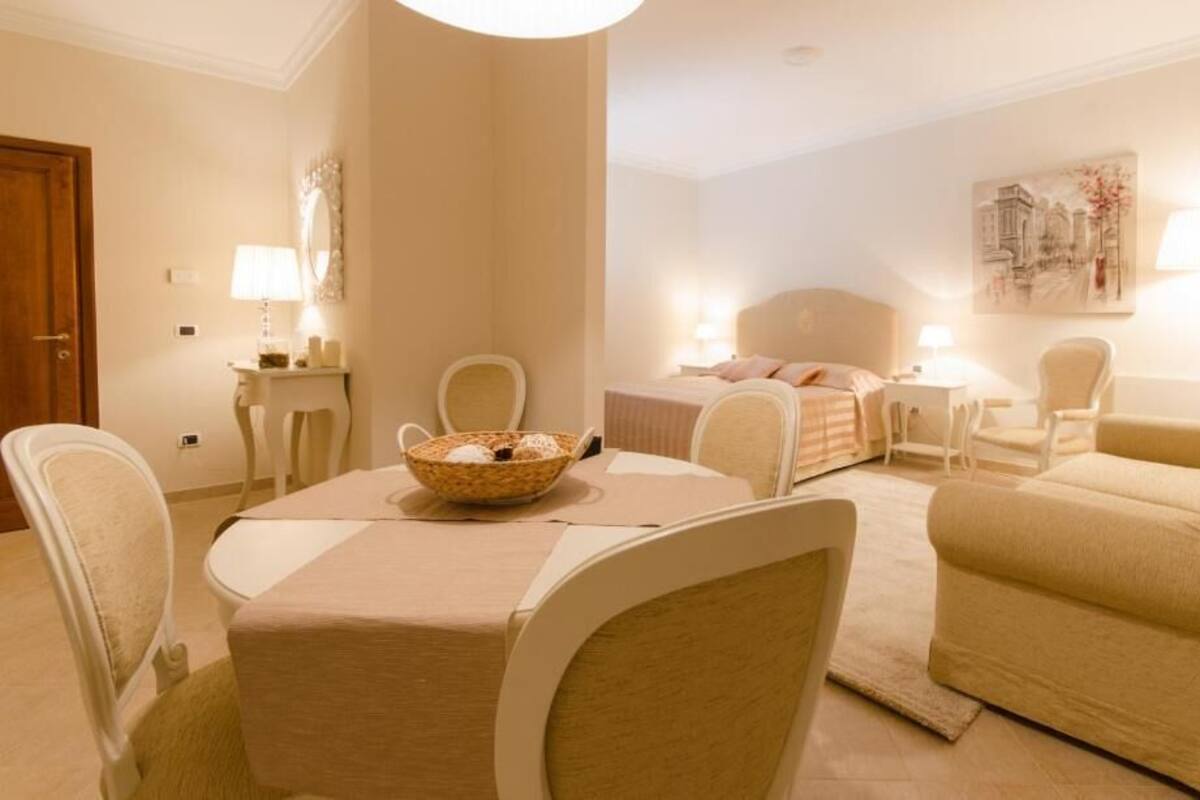 Een hotelkamer met een eettafel, twee stoelen, een bank, een bed en een nachtkastje met een lamp.