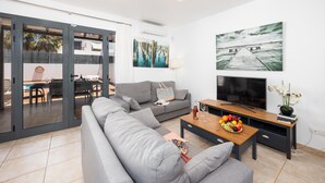 Ein modernes Wohnzimmer mit einem grauen Sofa, einem Couchtisch mit Früchten, einem Fernseher und Bildern an den Wänden.
