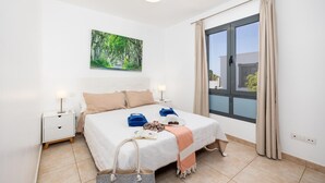 Ein Schlafzimmer mit einem Bett, Nachttischen, einem Gemälde, einem Fenster mit Vorhängen und Blick nach draußen.