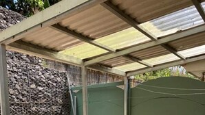 A covered patio area with a stone wall, a metal gate, and two wicker chairs around a small round table.