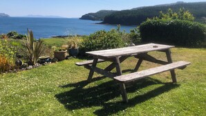 A wooden picnic table in a grassy area with a view of the sea and hills in the background.