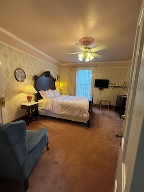Een slaapkamer met een bed, twee nachtkastjes met lampen, een plafondventilator, een televisie en een klein bureau met een stoel.