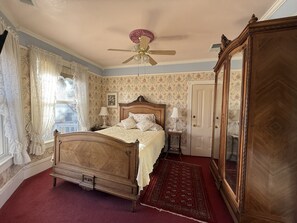 Een klassieke slaapkamer met een hemelbed, een plafondventilator en een grote spiegel.