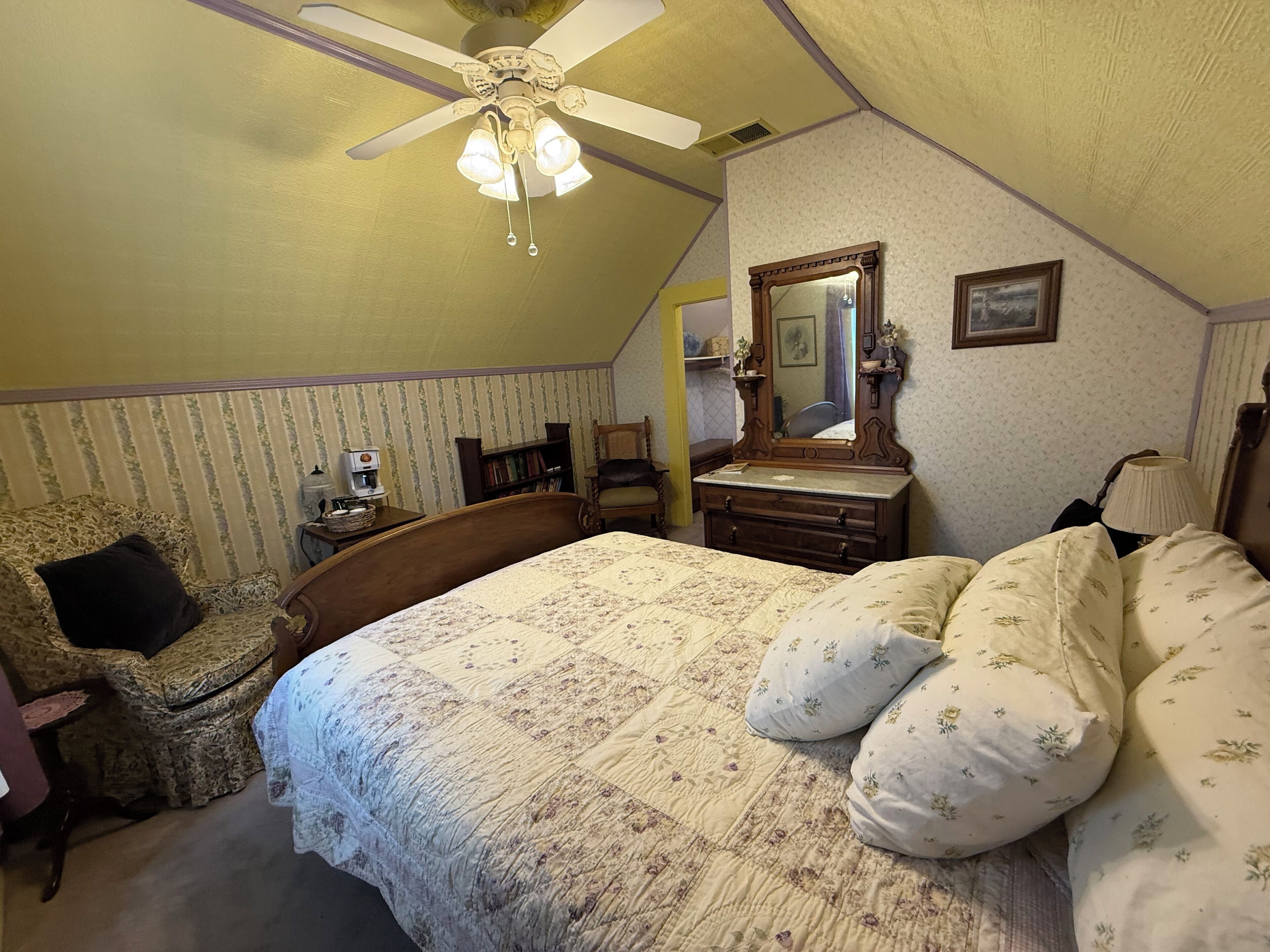 A bedroom with a bed, a chair, a dresser, a mirror, and a ceiling fan.