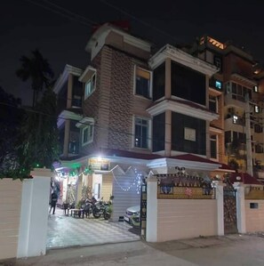 A multi-story building with a stone facade, a gated entrance, and a small outdoor seating area with tables and chairs. - Sree Sai Guest House (Guwahati)