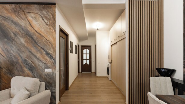 Un pasillo con pared de mármol, un sofá, una lavadora y un comedor con sillas y una mesa.