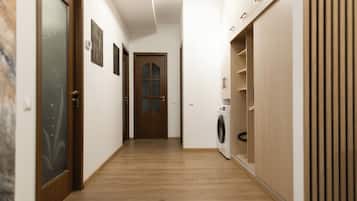 Un pasillo con suelo de madera, una puerta con vidrio esmerilado y una lavadora dentro de un armario empotrado.