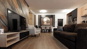 Una sala moderna con televisor de pantalla plana, un sofá, una mesa de comedor con sillas y un mural de un paisaje urbano.