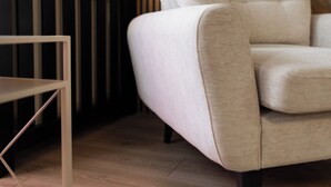 Un salón moderno con un sofá de color claro, suelo de madera, una consola negra y una pared con listones de madera verticales.