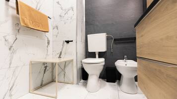 Un baño moderno con piso de mármol, inodoro, bidé y un mueble de madera.