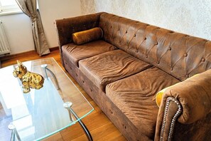 A brown leather sofa with a tufted backrest and a single cushion, positioned next to a glass coffee table with a golden figurine and a black object.