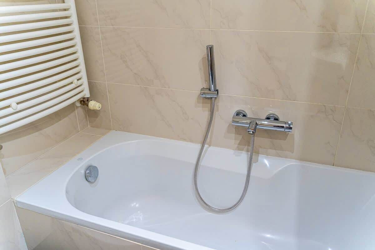 A modern bathroom with a white bathtub, a handheld showerhead, and a wall-mounted faucet.