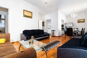 Una sala de estar moderna con un sofá negro, una mesa de centro de vidrio y un tapete estampado de leopardo. Hay una zona de comedor con una mesa y sillas, y una cocina al fondo.
