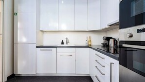 Une cuisine moderne avec des meubles blancs, un plan de travail noir et des appareils électroménagers en acier inoxydable, notamment une machine à café et un four.
