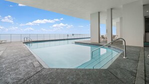 A modern indoor swimming pool with clear blue water, surrounded by a concrete deck and a glass barrier. - Windemere 1206 (Pensacola)