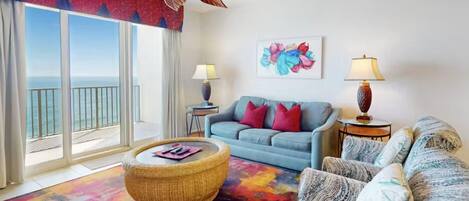 A living room with a sofa, armchairs, a coffee table, and a view of the ocean through large windows.