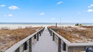 A wooden boardwalk leading to a beach with a tractor on the sand. - Shoalwater 1005 (Orange Beach)