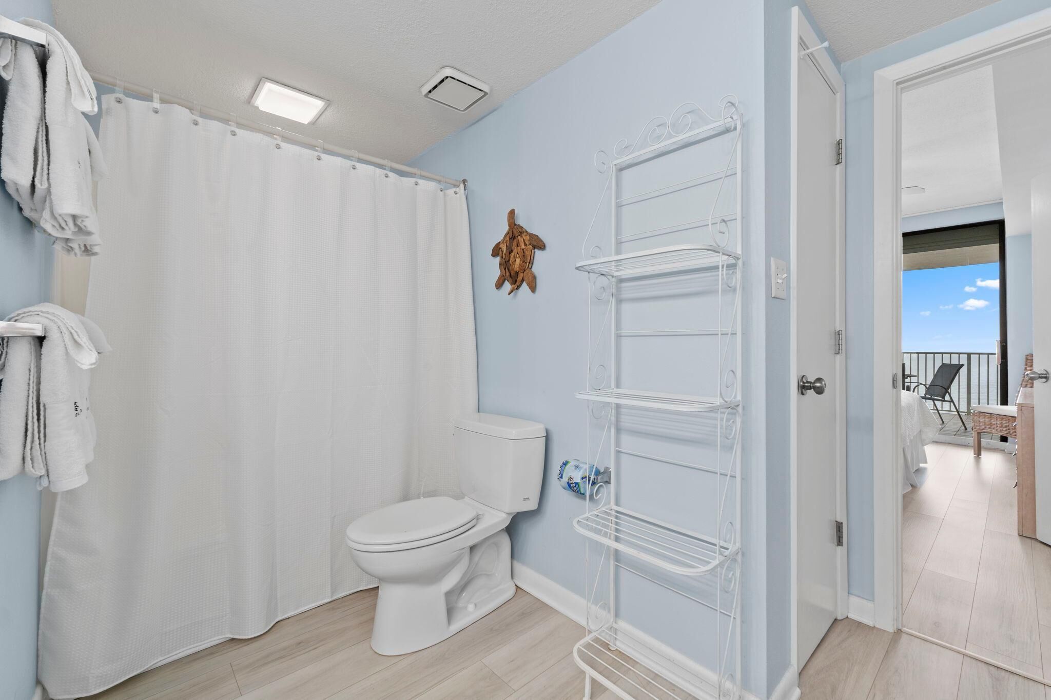 A bathroom with a toilet, shower curtain, and a white shelf unit.